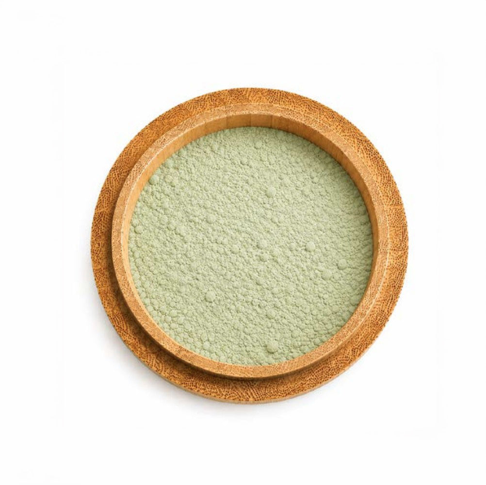 A top view of the clay face mask from the Christmas Self-Care Night In Gift Set, featuring matcha powder, contained in a round, shallow wooden bowl, on a white background.