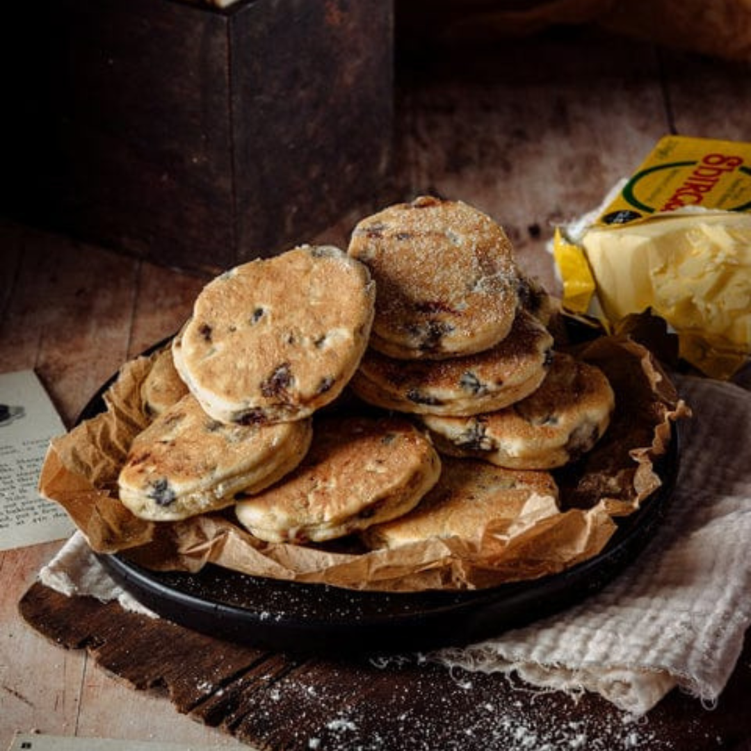 Stack of round Welsh Cakes made by Wilfreds, displayed on a dark plate with a rustic background.