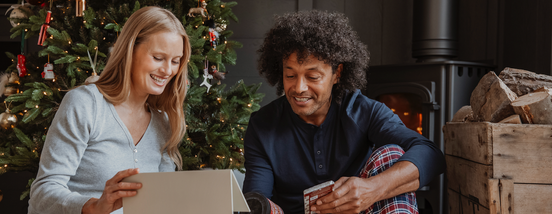 Couple sitting infront of Christmas tree opening gift hamper