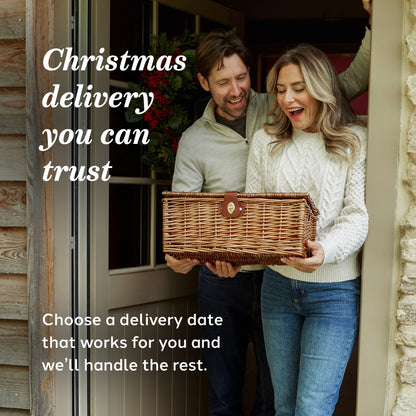 An informative image showing a smiling couple standing in a doorway holding a wicker basket. Large text reads 'Christmas delivery you can trust' with smaller text below.
