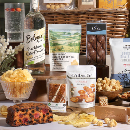 Classic alcohol-free gift basket, with sweet and savoury treats arranged around the willow basket, including salted caramel chocolate, nuts, flapjack, cake, fudge, and sparkling elderflower drink.