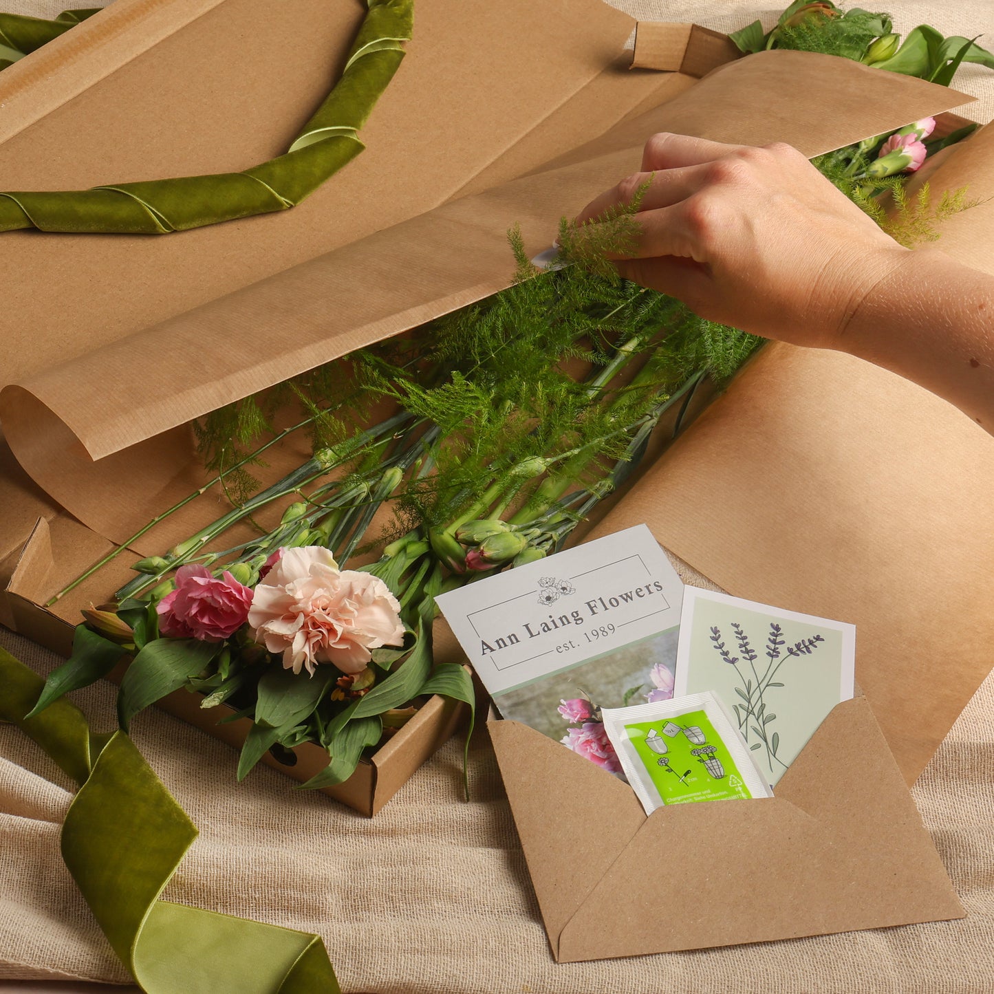 a hand is opening luxurious gift wrap to reveal the seasonal letterbox flowers and floral care pack inside