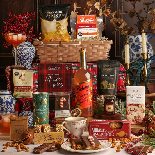 Luxury Joy of Christmas Hamper filled with assorted treats and snacks, including Yorkshire Crisps, sparkling clementine and cranberry, coffee, and Anna's Ginger Thins, arranged with mugs, chocolate, and festive decorations on a table.