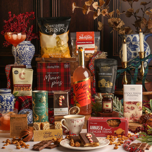 Luxury Joy of Christmas Hamper filled with assorted treats and snacks, including Yorkshire Crisps, sparkling clementine and cranberry, coffee, and Anna's Ginger Thins, arranged with mugs, chocolate, and festive decorations on a table.