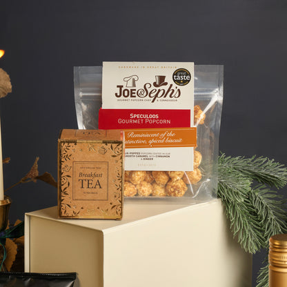 Joe & Seph's Gourmet Popcorn and Breakfast Tea box from the Luxury Festive Flavours Gift Box hamper displayed on a cream gift box against a dark grey background, featuring festive decorations.