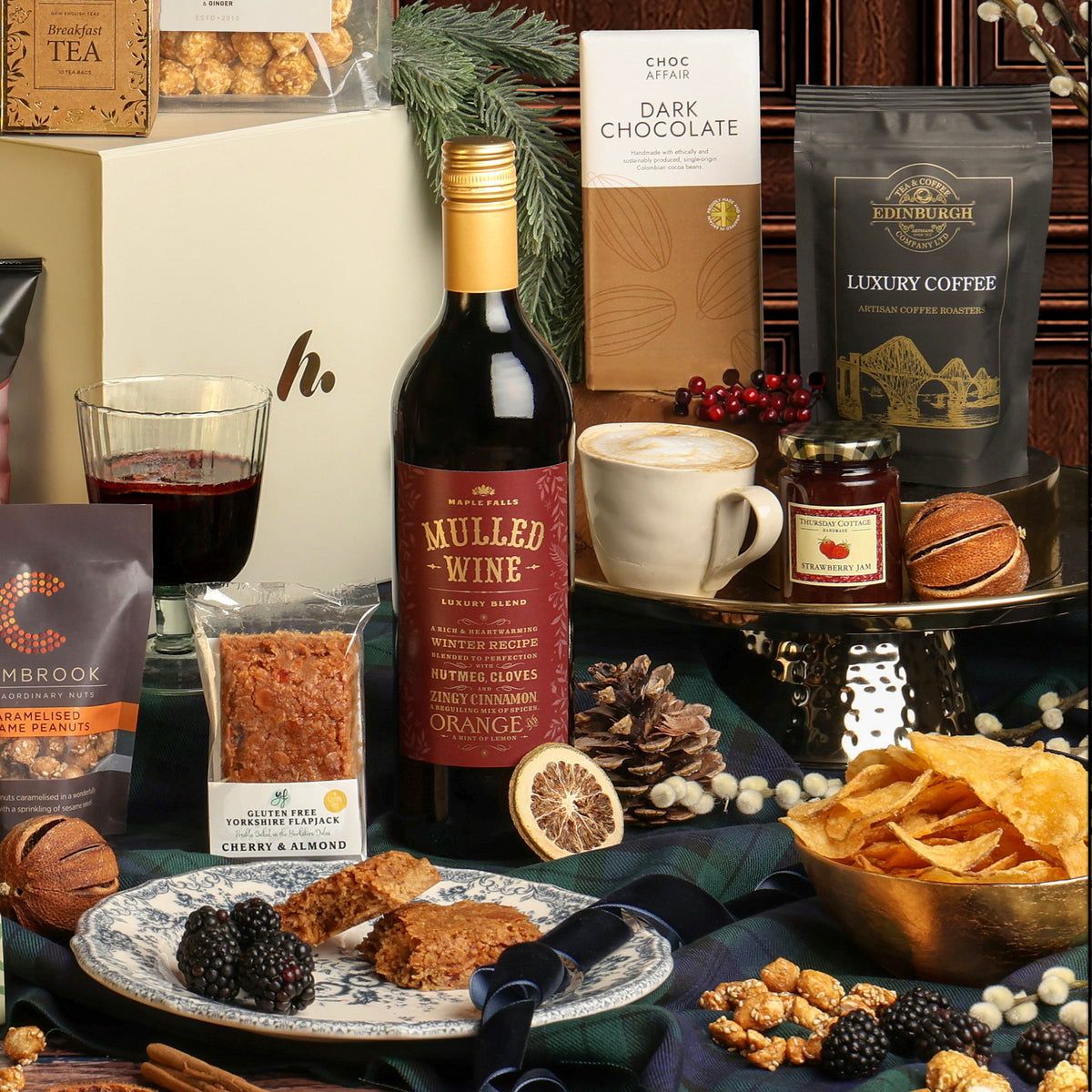 Luxury Festive Flavours Gift Box, with its contents displayed around the gift box, including mulled wine, crisps, coffee and chocolate, styled with a coffee cup and dried citrus decorations. 