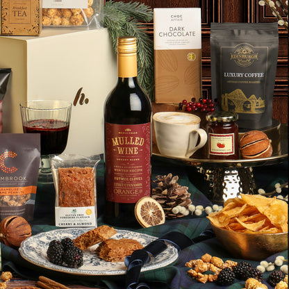 Luxury Festive Flavours Gift Box, with its contents displayed around the gift box, including mulled wine, crisps, coffee and chocolate, styled with a coffee cup and dried citrus decorations. 