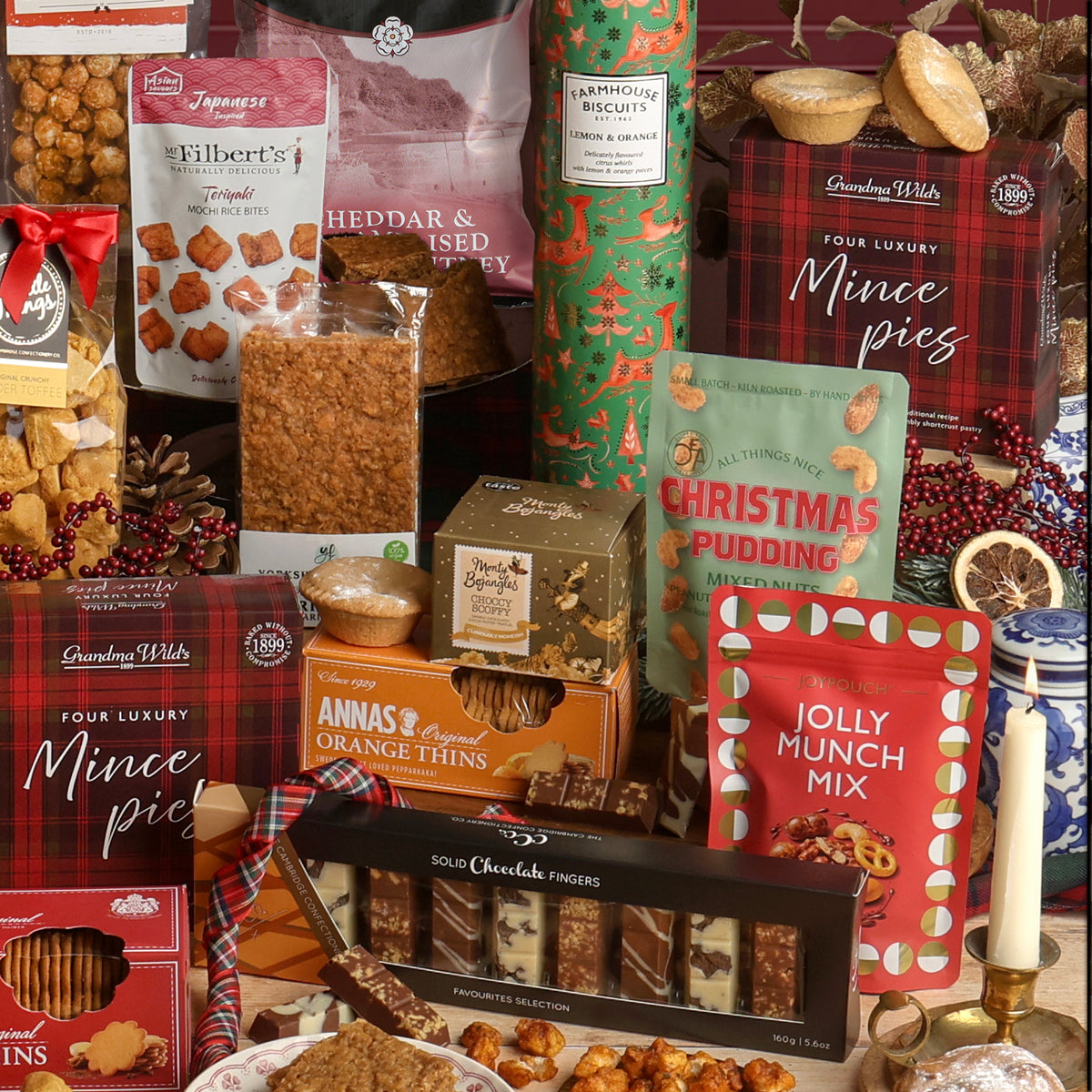 A festive assortment of Christmas snacks and treats arranged together, including mince pies, chocolate fingers, Orange Thins, Jolly Munch Mix, Christmas pudding mixed nuts, and more.