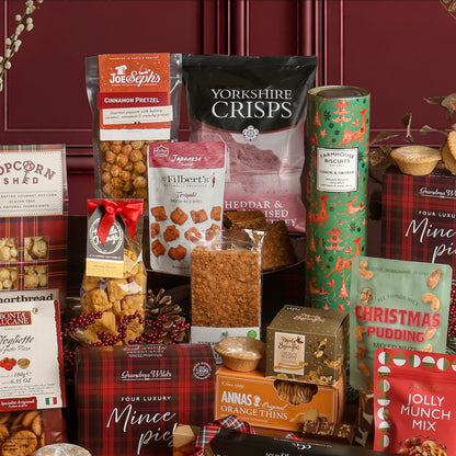 A Christmas Sharing Box featuring an assortment of packaged treats including Yorkshire Crisps, Jolly Munch Mix, mince pies, Christmas Pudding nuts, and various baked goods, arranged on a dark red wooden panel background.
