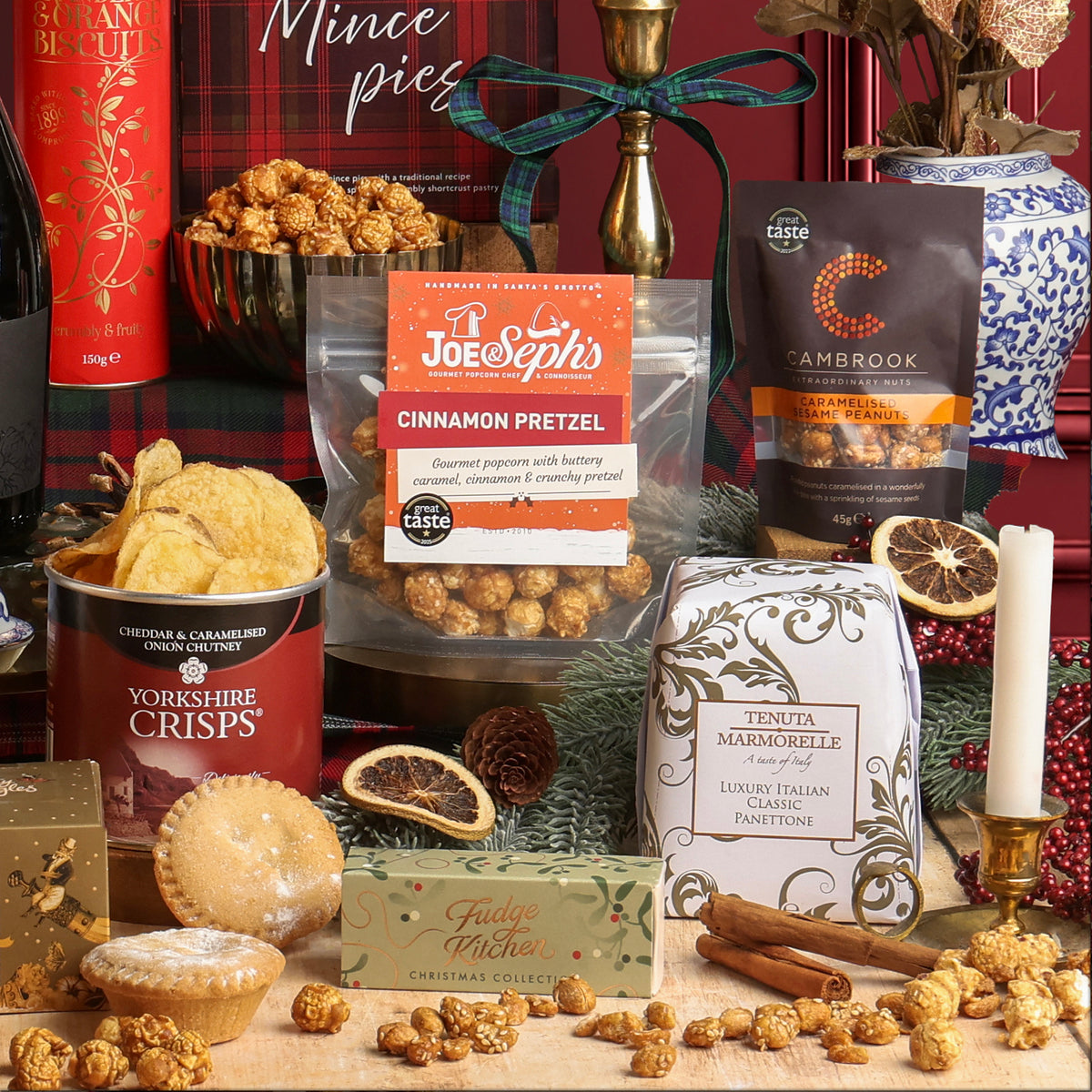 Holly Jolly Christmas Box featuring sweet and savoury food items, styled in a Christmas setting with plaid cloth, ribbon, candles, and festive decorations.