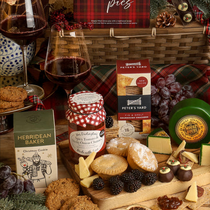 The Classic Christmas Food and Wine Hamper with festive food and drink, displayed around a bamboo basket, featuring sweet and savoury snacks, styled with cheese wedges, grapes, blackberries and wine glasses. 