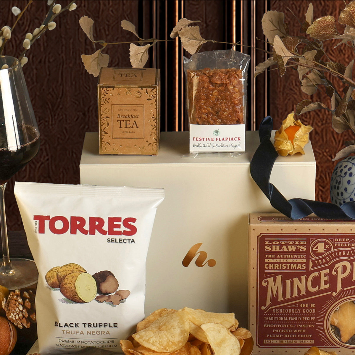 The Red Wine and Festive Treats Hamper, showing some of the items included, featuring tea, mince pies, crisps and a festive flapjack, displayed on top of the gift box.
