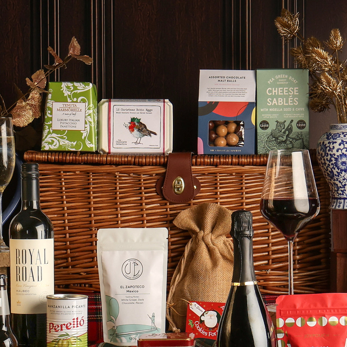 The Luxury Family Sharing Christmas Hamper arranged with its contents surrounding the hamper, styled with a glass of red wine. 