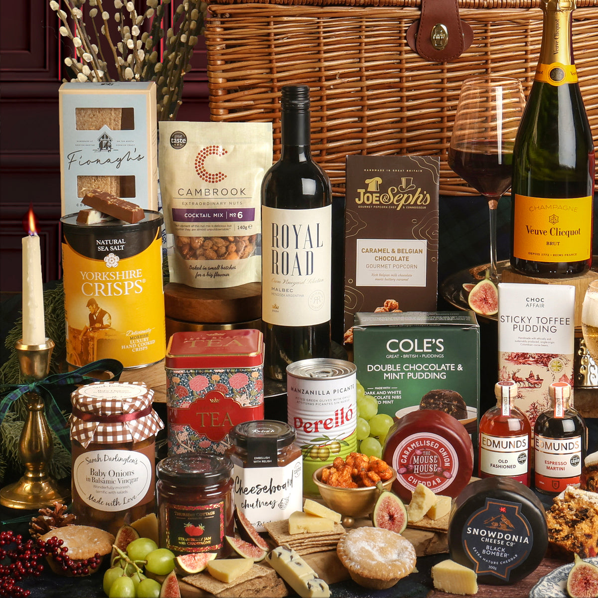 A luxury Christmas Celebration gift hamper filled with an assortment of premium snacks, cheeses, wines, and chocolates, arranged beautifully in front of a wicker basket.