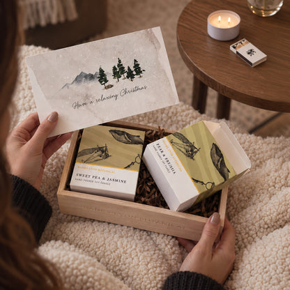 A wooden gift box opened to reveal two soy candles in a Christmas candle gift set, with a person holding the gift.