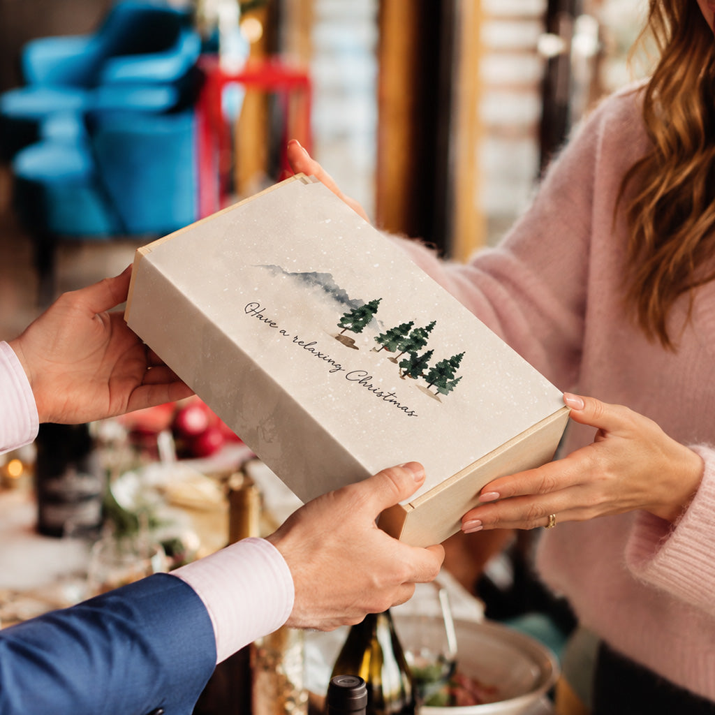 A person hands a Christmas candle gift set to another person.
