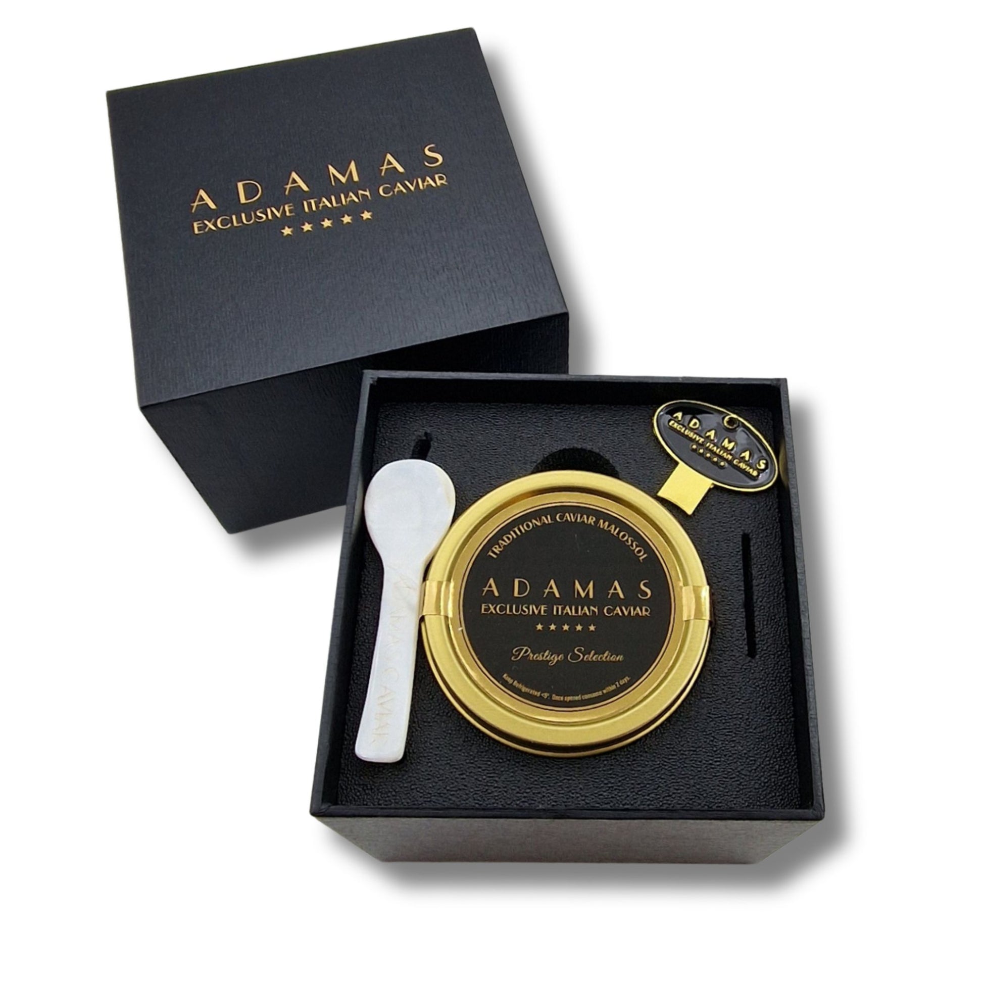 Adamas Italian Caviar gift set featuring a Prestige Selection tin of caviar, a mother of pearl spoon, and a tin opener, presented in a black gift box next to its matching lid.