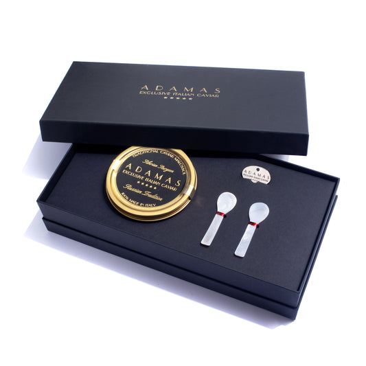 Adamas deluxe caviar gift set in a black presentation box, featuring a round tin of Prestige Selection caviar, two mother of pearl spoons, and a tin opener.