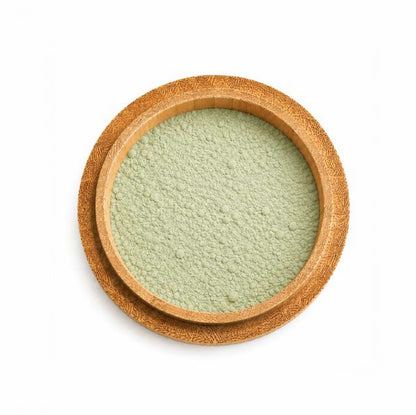A top view of the clay face mask from the Christmas Self-Care Night In Gift Set, featuring matcha powder, contained in a round, shallow wooden bowl, on a white background.