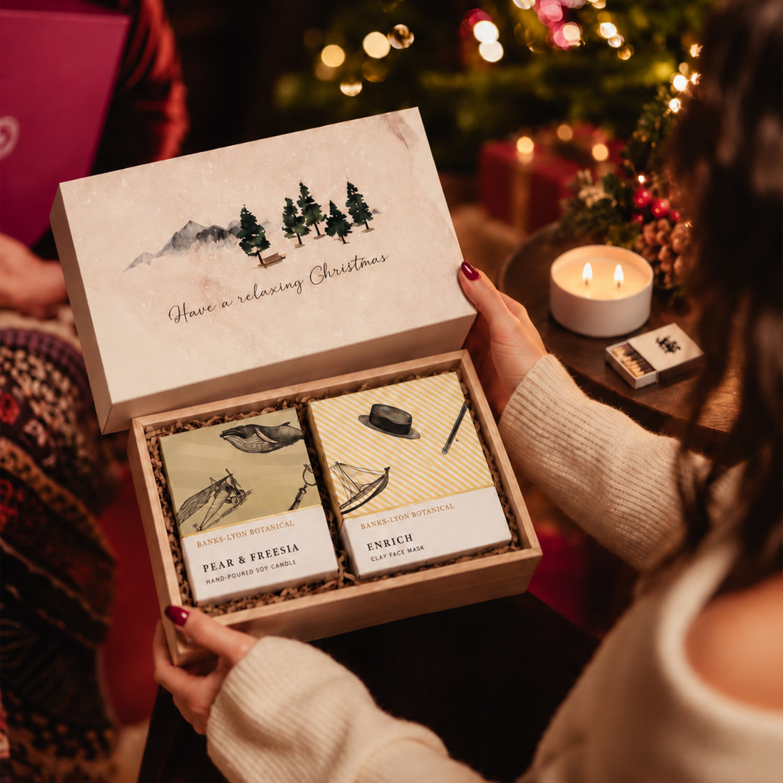 A person holds an open wooden gift box with Christmas illustrations, with two self-care products inside, set against a cosy Christmas themed background.