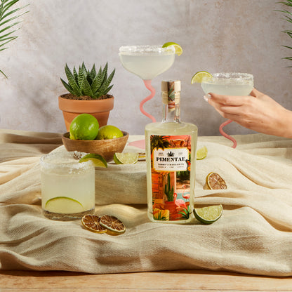 Pimentae tequila bottle with margaritas and limes on a tablecloth.