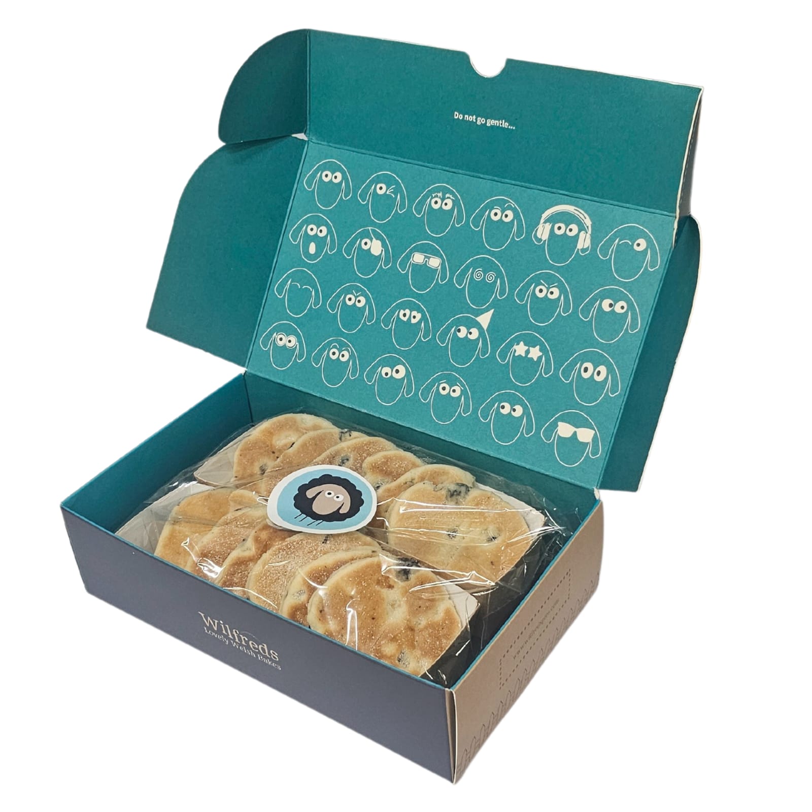An open teal and navy gift box containing several packaged round Welsh Cakes. The inside lid is decorated with white cartoon sheep faces, and the box has the brand name 'Wilfreds' visible on the front panel.