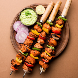 Three tandoori chicken kebabs on a plate with chutney and onions