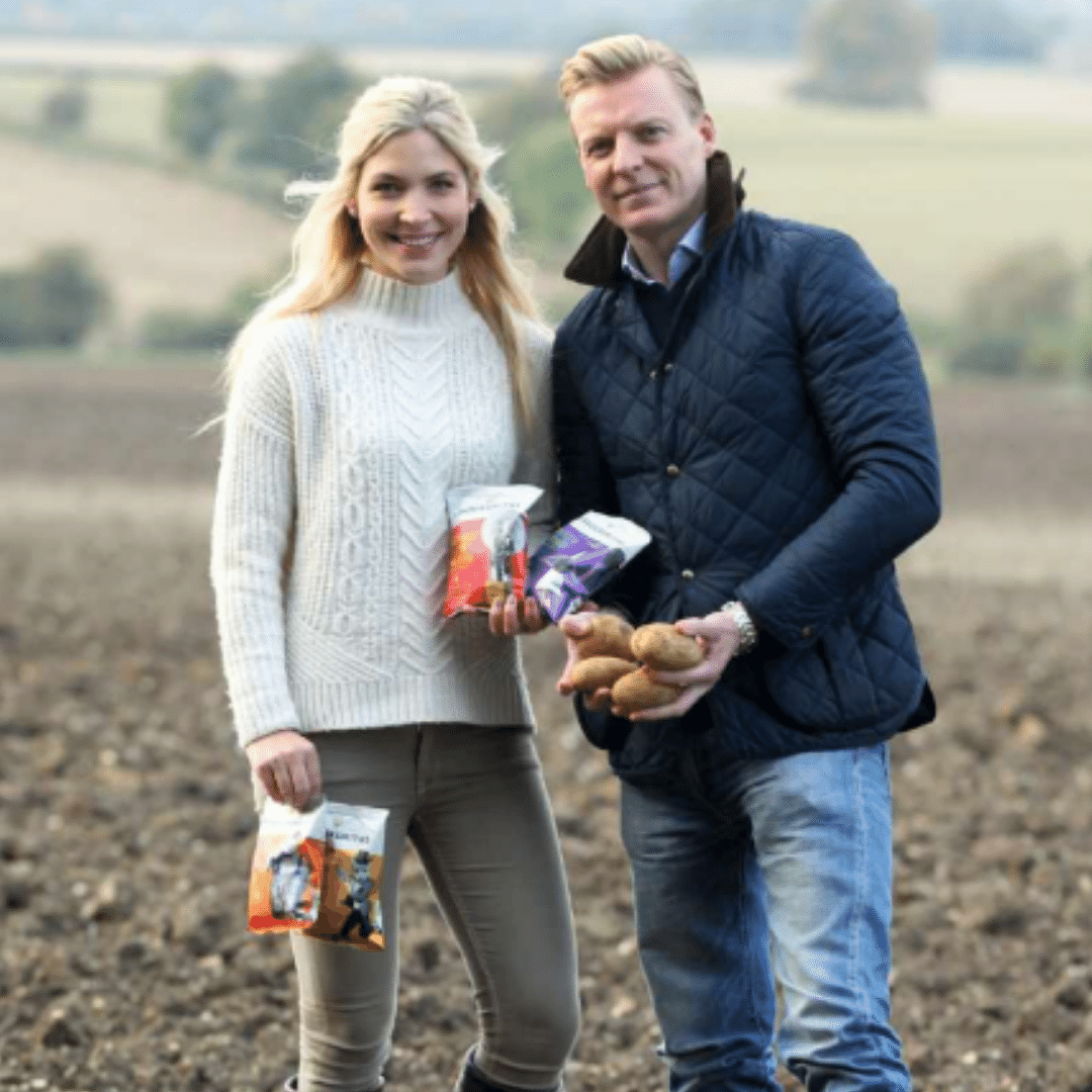 Owners Mike and Collette in a field with their homegrown potatoes and packets of Savoursmiths crisps