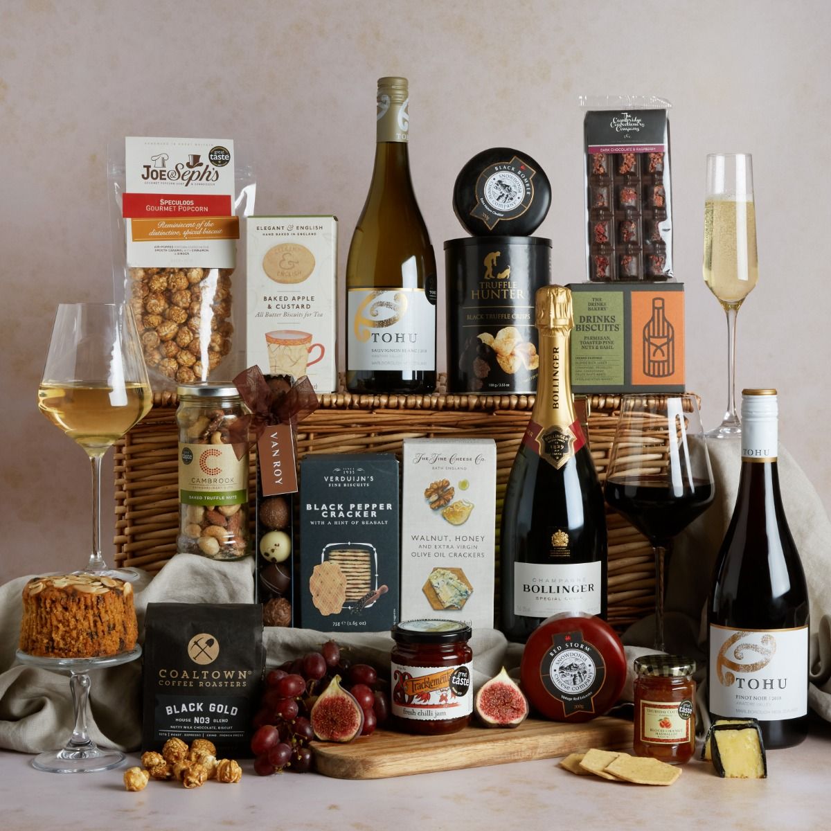 The Deluxe Hamper with contents on display and glasses of red and white wine, with wicker basket