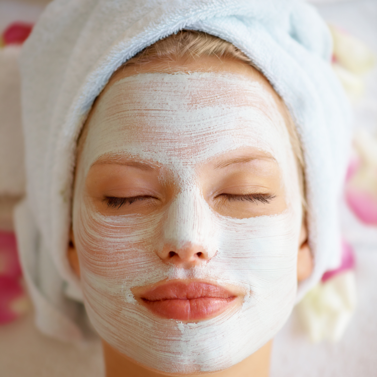 A woman with her hair wrapped in a towel, eyes closes and with a face mask on having a pamper session