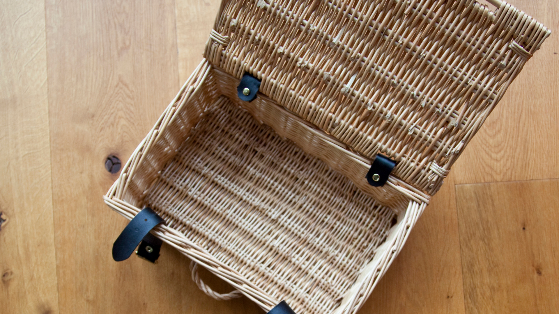 Open and empty wicker basket with lid on wooden floor