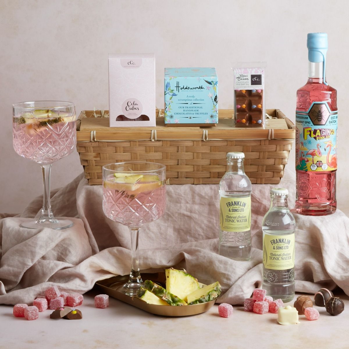 The Flagingo pink gin hamper with contents on display, a G&T in a glass and with its wicker basket