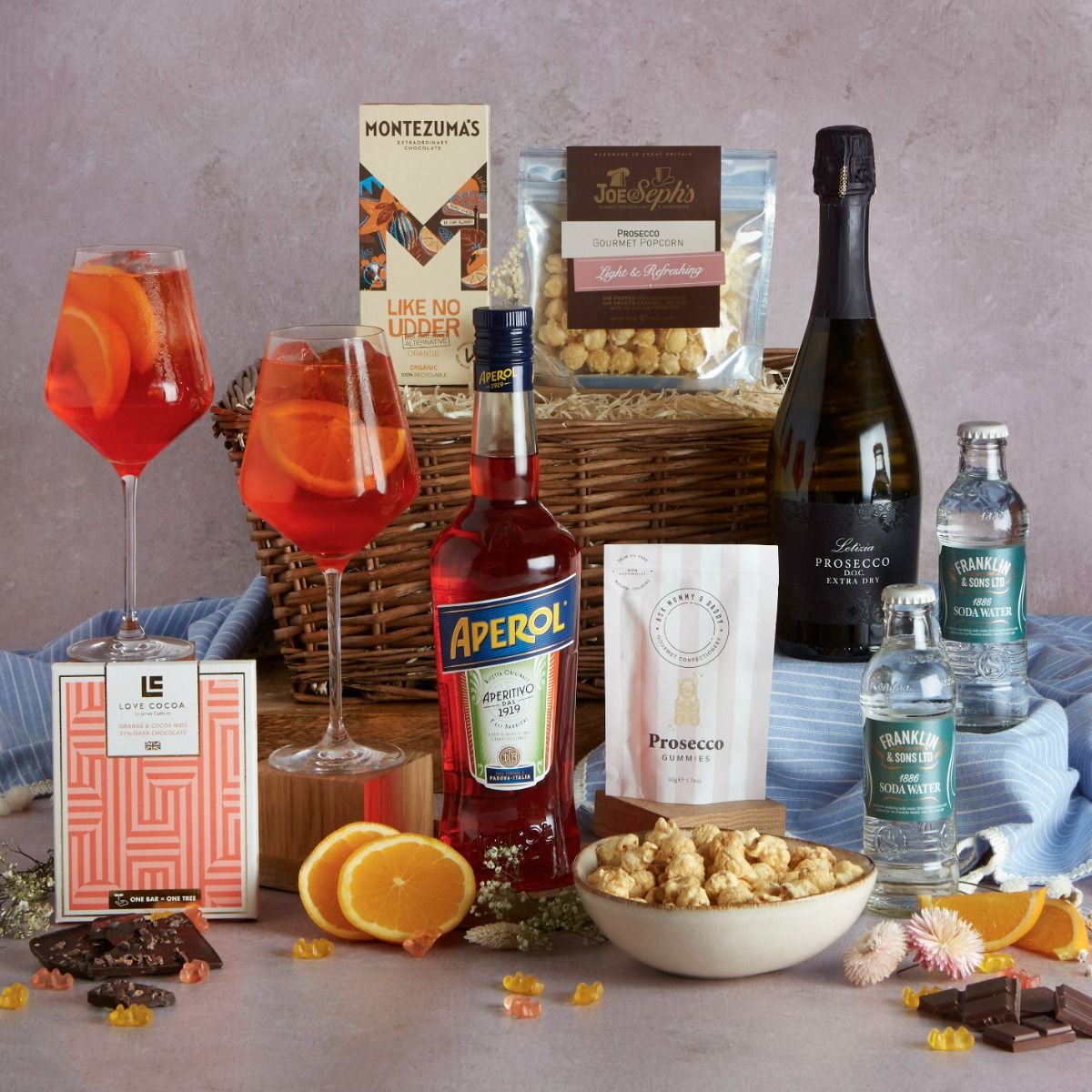 Aperol Spritz Summer Hamper with contents on display and two cocktail glasses of Aperol