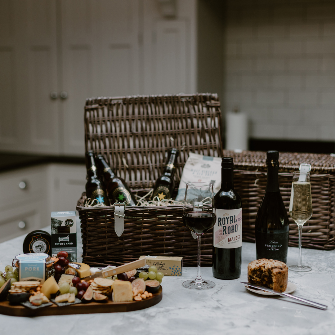 Open hamper with a selection of beverages, cake and a platter of cheese